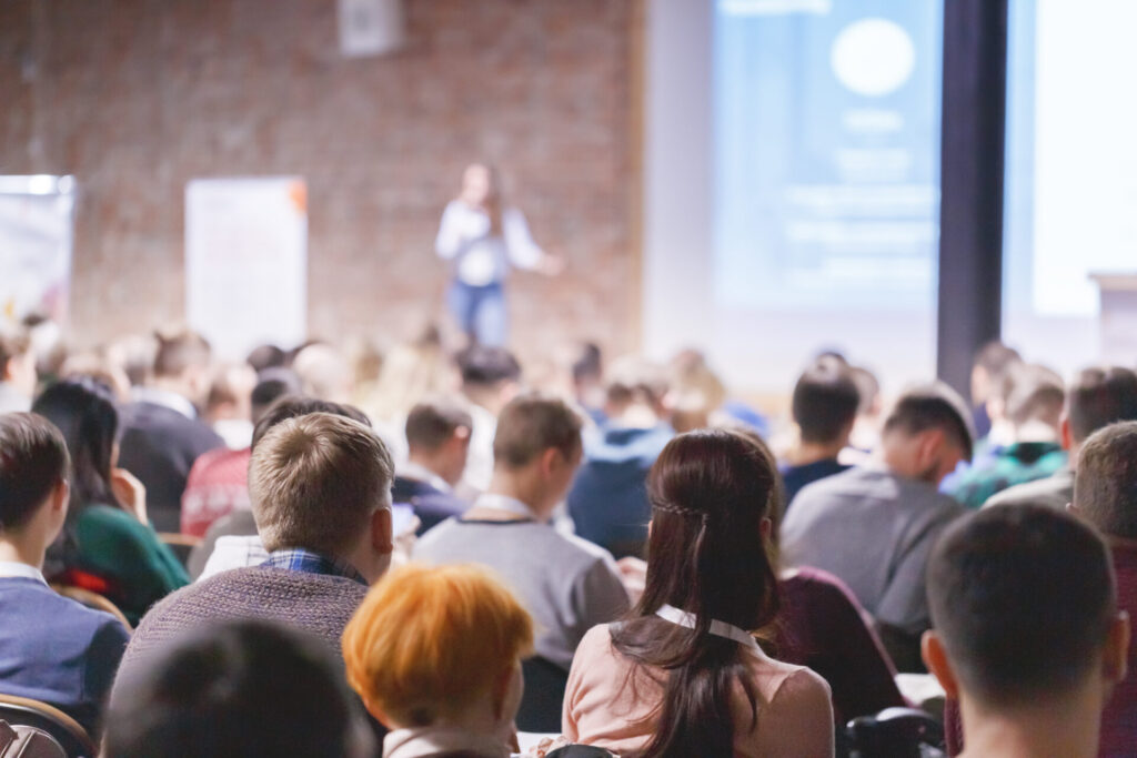 Adult students listen to professor's lecture in room, hands up for queue of asking question to Lecturer or poll voting. Rear view, Audience Watching a Presentation. Business, education.